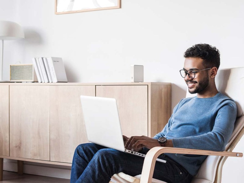 mann sitzt in einem Stuhl im wohnzimmer, er hat einen Laptop auf dem Schoß