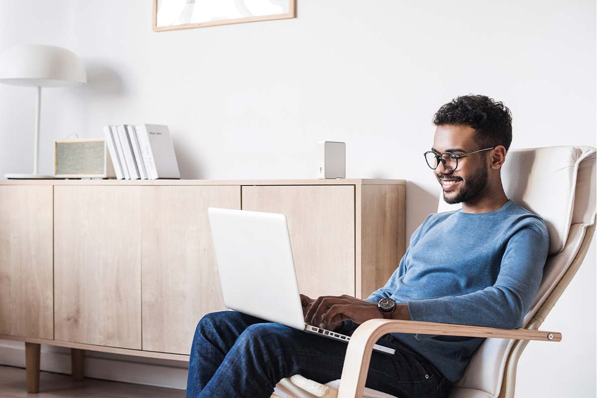 mann sitzt in einem Stuhl im wohnzimmer, er hat einen Laptop auf dem Schoß