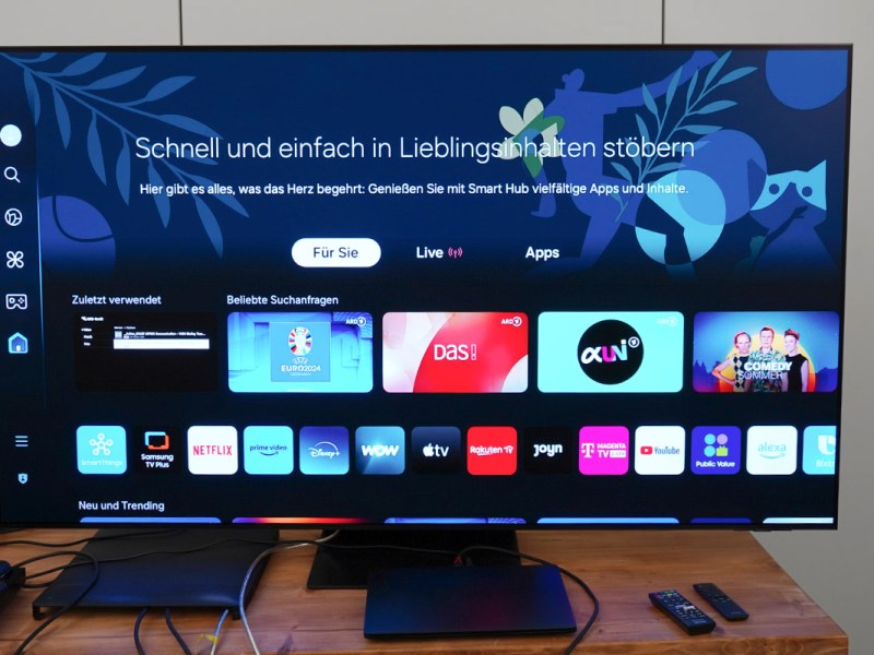 Ein Smart-TV Samsung Galaxy S95D steht eingeschaltet auf einem Holztisch.