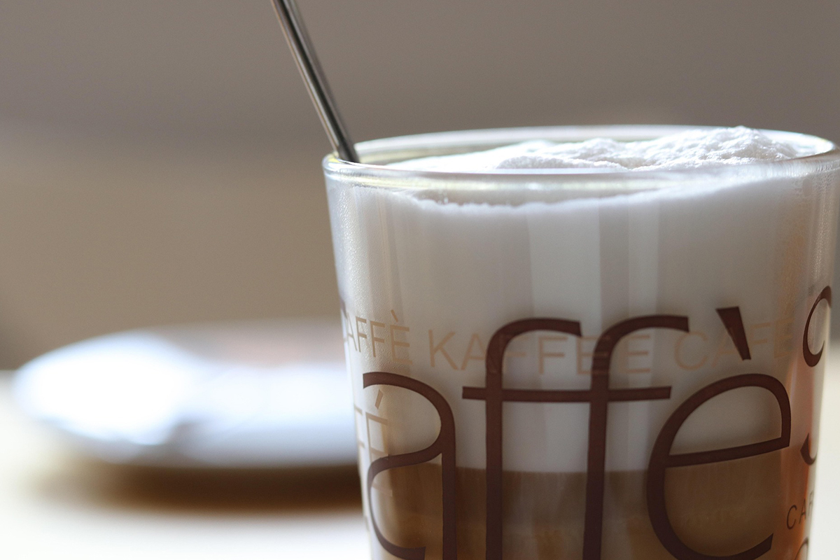 Ein Glas mit Milchschaum und Kaffee im Vordergrund.