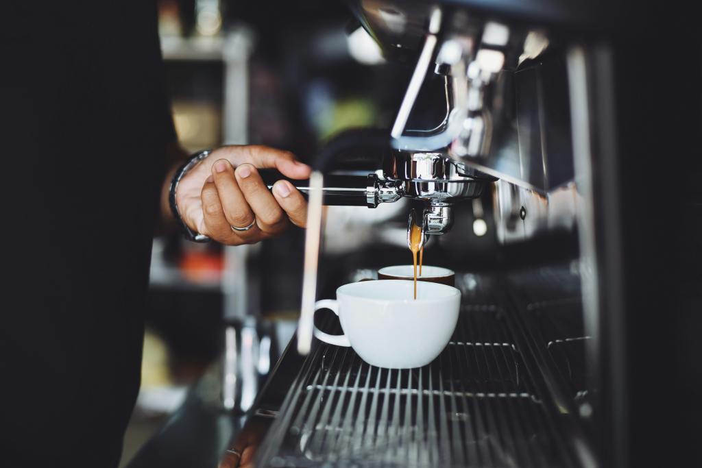 Eine Person bedient eine große Siebträgermaschine, Espresso läuft in weiße Tassen.