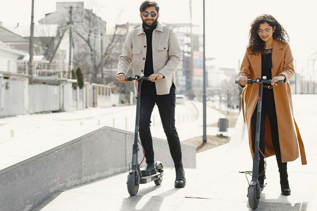 Zwei Personen fahren nebeneinander auf einem E-Scooter auf die Kamera zu