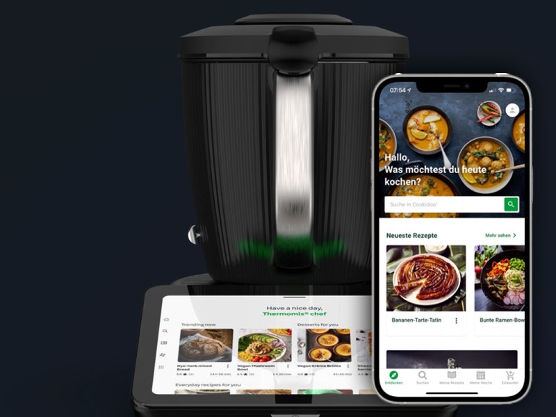 Thermomix TM7 im Hintergrund, vorne ein Smartphone mit geöffneter Cookidoo-APp