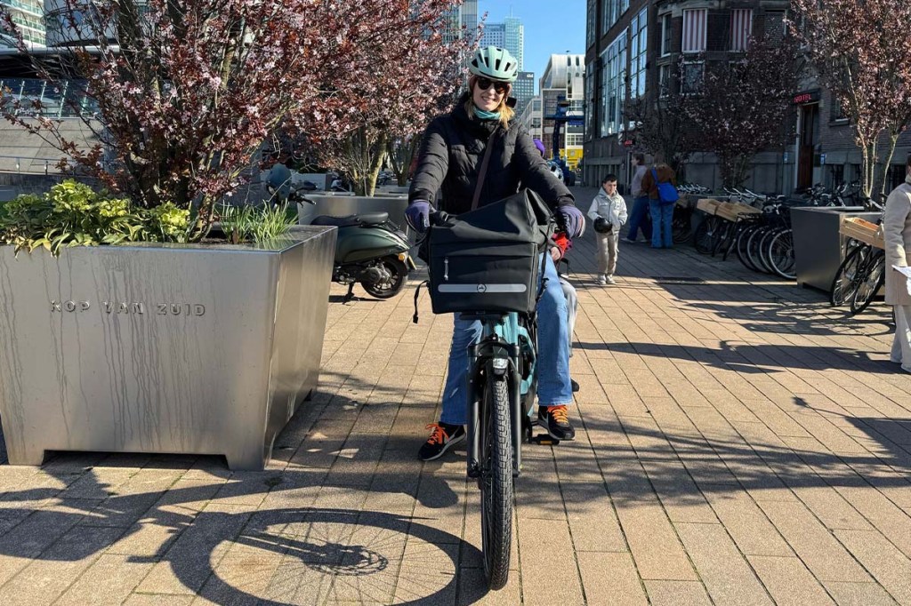 Frau fährt mit einem E-Bike auf die Kamera zu, sie ist umgeben von blühenden Bäumen